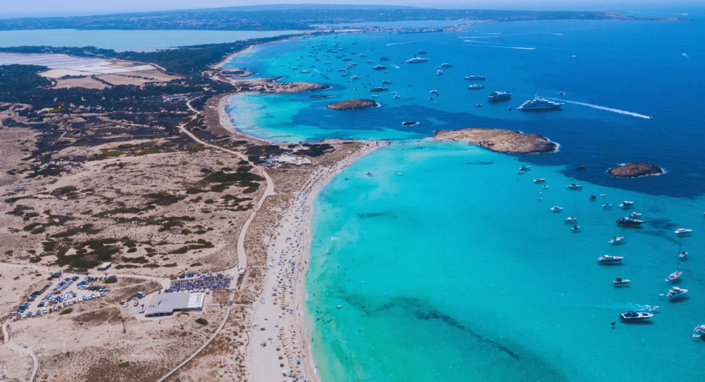 A stunning aerial perspective of the turquoise waters and white sands of Illetes Beach Formentera, Formentera, with a multitude of boats creating a vibrant scene.