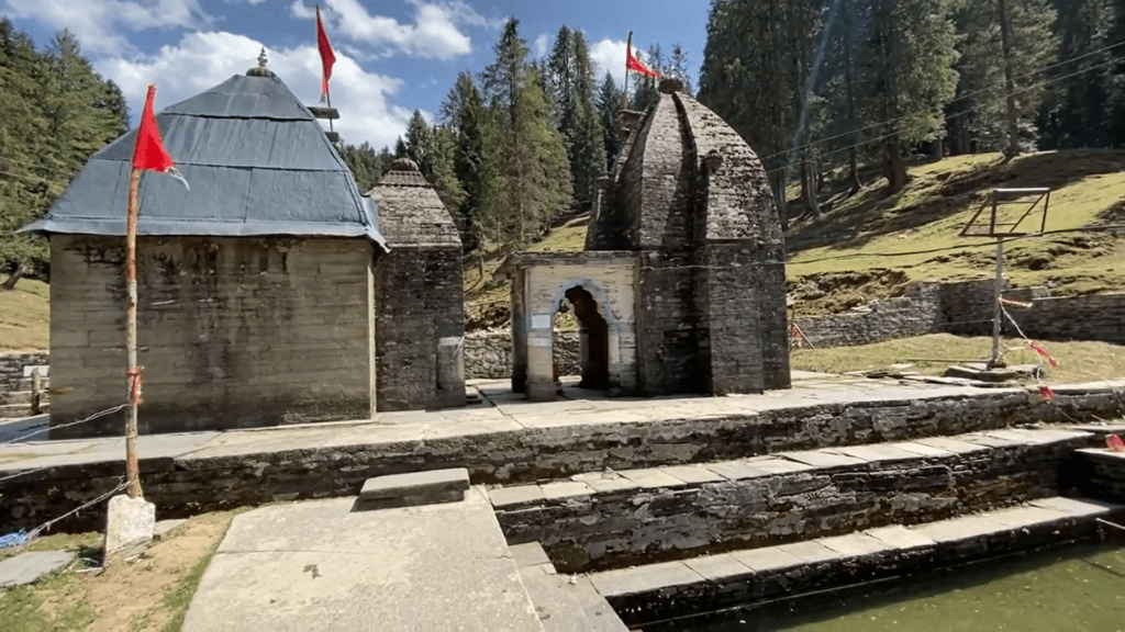 Giri Ganga Temple, a centuries-old Hindu shrine located in Giri Ganga, Himachal Pradesh. The temple features a unique pyramidal roof and a stone-walled courtyard, with a sacred pond and surrounding pine forests.