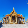 "The grand Wat Phra Kaew temple with golden spires and intricate architectural details, located in Bangkok, Thailand, under a clear blue sky."